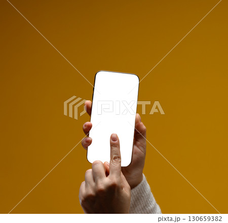 Close-up of female hands holding modern smartphone with blank white screen. Yellow background. Mock up Close-up of female hands holding modern smartphone with blank white screen. Yellow background. Mock up 130659382