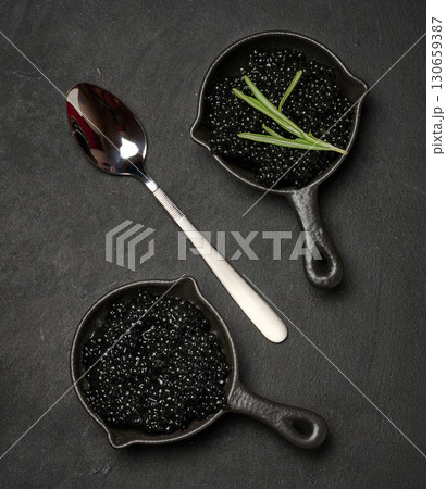 Top view of a small black cast iron skillet filled with black caviar, garnished with two sprigs of fresh rosemary. 130659387