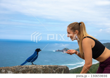 Woman meets bird on cliff with ocean view, travel vibe Woman meets bird on cliff with ocean view, travel vibe 130659698