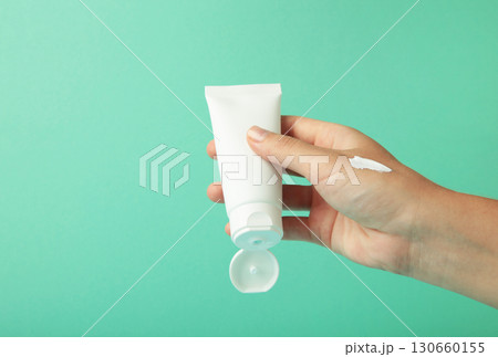 Hand holding blank white plastic tube on mint background. Hand holding blank white plastic tube on mint background. 130660155