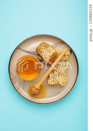 Bowl of sweet honey, dippers and combs on plate on blue background. Vertical photo 130660159
