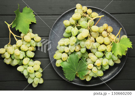 Green grape with leaves on dark plate on black background. 130660200