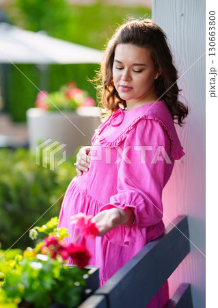 Beautiful young pregnant woman in pink dress on summer veranda. Beautiful young pregnant woman in pink dress on summer veranda. 130663800