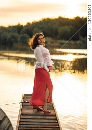 Beautiful young pregnant woman in red dress at sunset on the riverbank Beautiful young pregnant woman in red dress at sunset on the riverbank 130663801