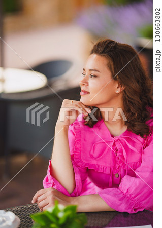 Beautiful brunette young woman in bright pink dress at summer cafe table. Beautiful brunette young woman in bright pink dress at summer cafe table. 130663802