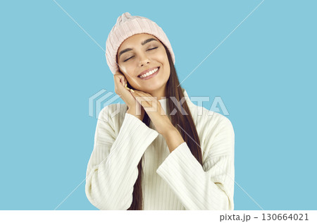 Portrait of happy, beautiful, smiling, young woman in white sweatshirt and warm knitted hat on an isolated blue background Portrait of happy, beautiful, smiling, young woman in white sweatshirt and warm knitted hat on an isolated blue background 130664021