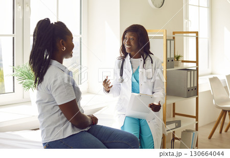 Friendly African American female doctor explaining symptoms and diagnosis to her female patient. Friendly African American female doctor explaining symptoms and diagnosis to her female patient. 130664044