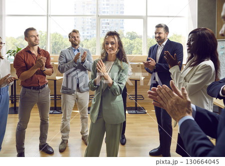 Smiling woman and business leader with team of people applauding in office. Smiling woman and business leader with team of people applauding in office. 130664045