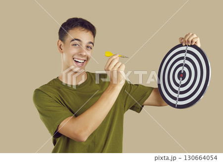 Happy teenage boy focuses on achieving his goals and aims little arrow at target board 130664054