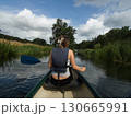 A young woman seen from behind canoeing in a river. Dark summer clouds in the background 130665991