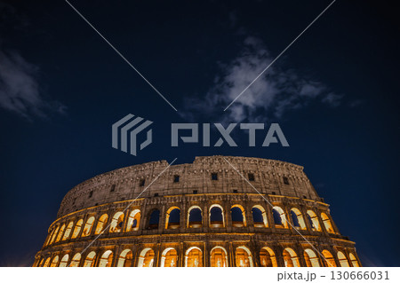 Colosseum illuminated at night with glowing arches under dark blue sky Colosseum illuminated at night with glowing arches under dark blue sky 130666031