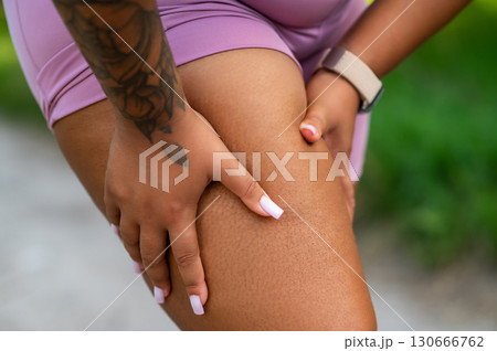 Closeup of African American woman in pink sportswear touching leg with hands 130666762