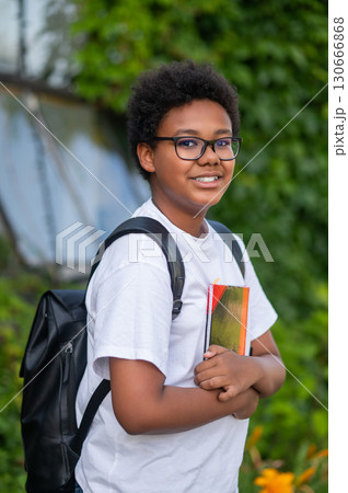 Dark-skinned curly-haired teen with a backpack and a book in his hands Dark-skinned curly-haired teen with a backpack and a book in his hands 130666868