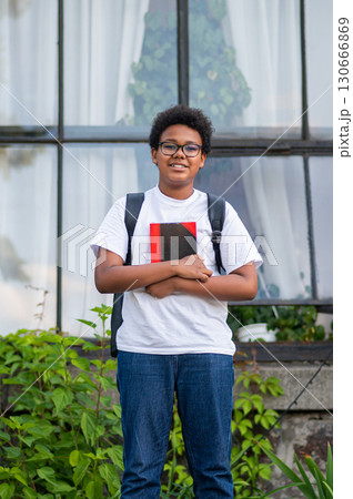 Dark-skinned curly-haired teen with a backpack and a book in his hands 130666869