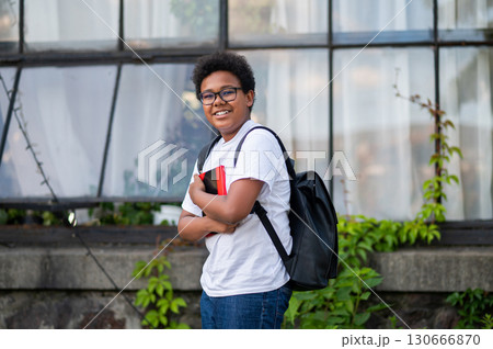 Dark-skinned curly-haired teen with a backpack and a book in his hands Dark-skinned curly-haired teen with a backpack and a book in his hands 130666870