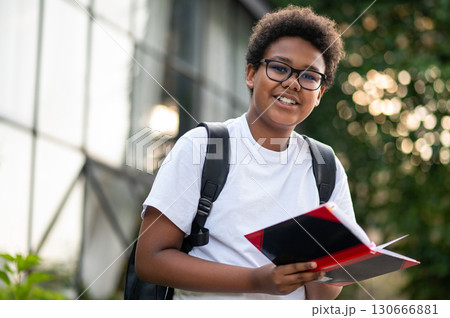 African american boy in eyeglasses with a book in hands looking involved and focused 130666881