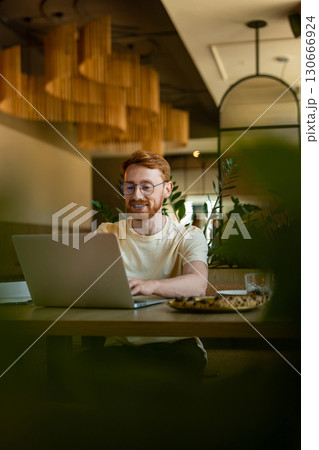 Ginger young adult in glasses working on laptop during lunch Ginger young adult in glasses working on laptop during lunch 130666924