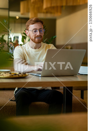 Ginger man professional using laptop at restaurant with pizza Ginger man professional using laptop at restaurant with pizza 130666926