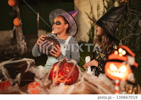 Two young girls wearing witch costumes celebrating Halloween with carved pumpkins 130667019