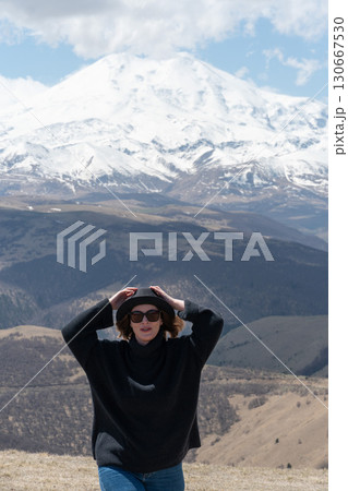 Woman in black sweater and hat enjoys panoramic view of snow-covered Mount Elbrus under a dramatic sky Woman in black sweater and hat enjoys panoramic view of snow-covered Mount Elbrus under a dramatic sky 130667530