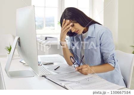 Tired woman suffering from headache sitting at the desk on her workplace in office. 130667584