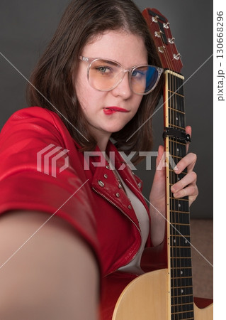 Female influencer guitarist biting her lip in playful expression takes selfie of herself with guitar in her hand, creating user-generated content 130668296