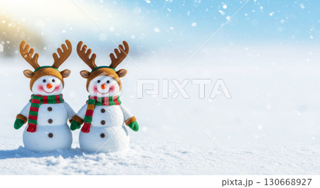 Two adorable snowmen in reindeer hats and scarves stand in a snowy landscape. Christmas and New Year. 130668927