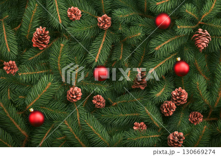 Vibrant green fir tree branches form a beautiful background, adorned with many natural brown pine cones and bright red Christmas ornaments for the holiday season. 130669274