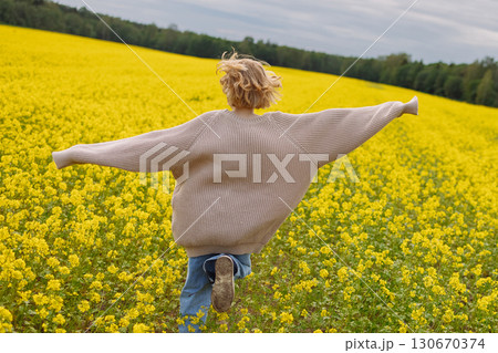 Rear view of 10 year old girl in beige sweater running in yellow rapeseed field 130670374