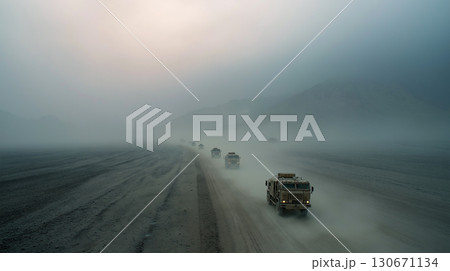 Multiple large vehicles slowly progress along a winding road shrouded in fog. The atmosphere appears thick and desolate, emphasizing the remote and isolated environment during early morning. 130671134