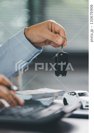 Business office, woman employee finalizes deal with client, handing over car key after signing contract and reviewing insurance and loan documents for sale or rent of vehicle at table. Business office, woman employee finalizes deal with client, handing over car key after signing contract and reviewing insurance and loan documents for sale or rent of vehicle at table. 130676906