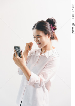 Asian woman rejoicing, looking happy, champion, fist pump gesture, standing over white background. young woman had happy, positive expression on her face, highlighted by bright smile. 130677303