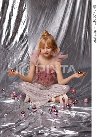 Smiling blonde girl in pink dress sitting with Christmas balls on silver background 130677549