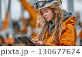 Female engineer using digital tablet at construction site, inspecting heavy machinery 130677674