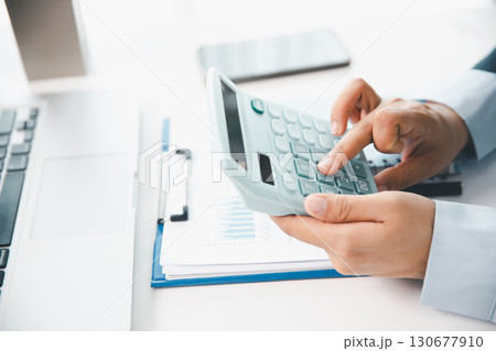 Accountant working on desk using calculator for calculate finance report in office. business finance, calculate tax by organizing financial documents, tracking income investment, accounting by hand. 130677910