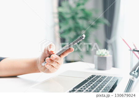 Close-up scene, a female seated at a table holds a smartphone, spending time on modern e-date services and social media through a mobile app, illustrating the wireless concept of digital usage. 130679024