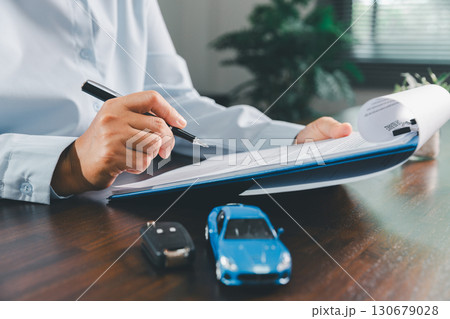 Customer signing insurance document lease agreement table, writing signature contract buying selling new or used vehicle, with car keys, warranty papers, guarantee included in transaction. 130679028