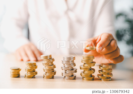 Hand places coin into saving jar, representing how smart finance, investment, banking practices turn money, cash, currency into financial wealth drives business growth and strengthens the economy. Hand places coin into saving jar, representing how smart finance, investment, banking practices turn money, cash, currency into financial wealth drives business growth and strengthens the economy. 130679342