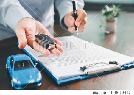 Customer signing insurance document lease agreement table, writing signature contract buying selling new or used vehicle, with car keys, warranty papers, guarantee included in transaction. 130679417