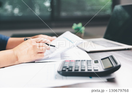 Office businesswoman hand to operate calculator analyzing financial data, counting costs on desk. accounting, financial analysis for business budget planning, calculation support, finance management. Office businesswoman hand to operate calculator analyzing financial data, counting costs on desk. accounting, financial analysis for business budget planning, calculation support, finance management. 130679768