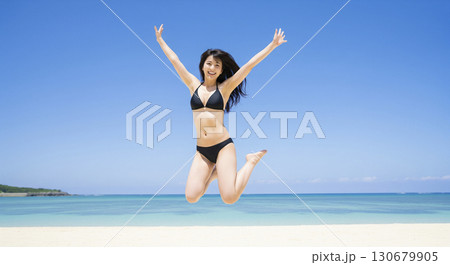 ビキニの女性　両手を広げて空を背景にジャンプする元気な姿 130679905