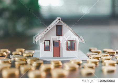 Model house, stacks of coins, calculator, financial documents on a wooden desk represent real estate investment and mortgage planning, highlighting financial growth and strategic planning strategies. 130680008