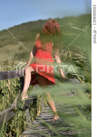 Woman in red dress standing barefoot on wooden footbridge in nature 130680083