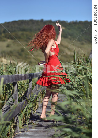 Woman in red dress standing barefoot on wooden footbridge in nature 130680084