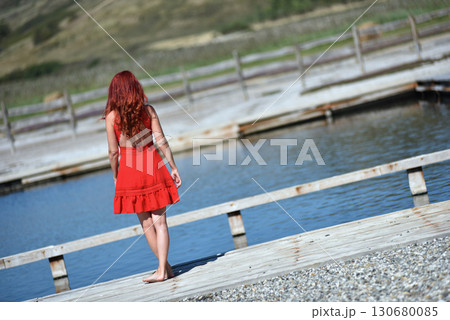 Back view of woman with red hair in red dress by pool Back view of woman with red hair in red dress by pool 130680085