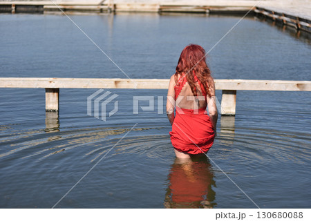 Back view of woman with red hair in red dress by pool 130680088