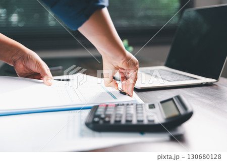 Office businesswoman hand to operate calculator analyzing financial data, counting costs on desk. accounting, financial analysis for business budget planning, calculation support, finance management. Office businesswoman hand to operate calculator analyzing financial data, counting costs on desk. accounting, financial analysis for business budget planning, calculation support, finance management. 130680128
