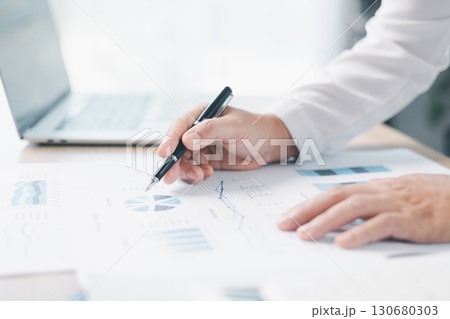 Businessman reviews financial reports, points on chart with pen while analyzing data at office desk working with calculator for accuracy. Concept of accounting, business planning, investment strategy. 130680303