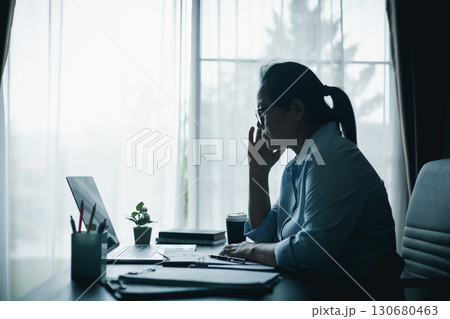 Stressed businesswoman working late at home office, feeling exhausted while reviewing financial documents on laptop. Concept of work stress, burnout, deadline and overwork. Stressed businesswoman working late at home office, feeling exhausted while reviewing financial documents on laptop. Concept of work stress, burnout, deadline and overwork. 130680463