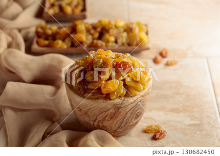 Yellow sultana raisins in a wooden bowl on a beige background. Yellow sultana raisins in a wooden bowl on a beige background. 130682450